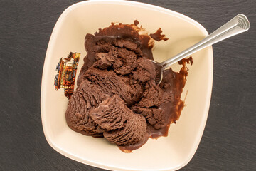 Chocolate ice cream in a ceramic bowl with a spoon on a slate stone, macro, top view.