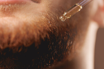 Young man holding pipette with oil for beard hair. Concept spa cosmetic and treatment wellness and...