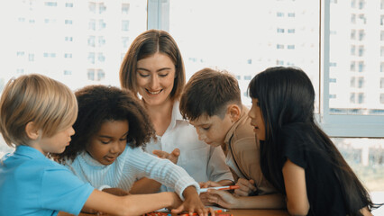 Fototapeta premium Professional caucasian teacher telling story to diverse student while sitting at table with storybook and colored book. Smart learner listening story while colored picture from instructor. Erudition.