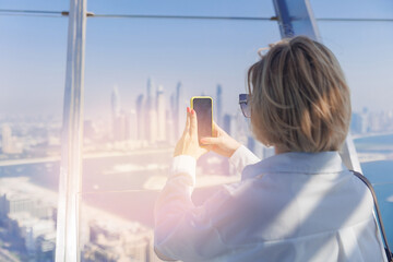 Young tourist woman shooting on mobile phone modern skyscraper in point view of Dubai sky building,...