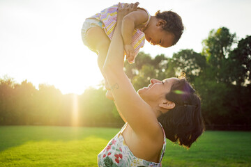 mother holding happy baby daughter in the air at sunset at the park outdoors in nature .concept of...