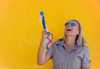Mature woman laughing and holding a snorkel with a yellow wall