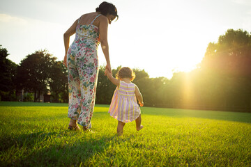 Mother and little daughter walking together in a park outdoors at sunset. evocative scene, concept...