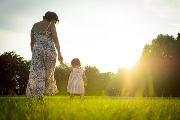 Mother and little daughter walking together in a park outdoors at sunset. evocative scene, concept...