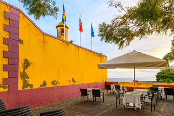 A small sidewalk cafe with sea views at the 17th century Fortress of São Tiago, or Funchal Fort along the seafront of the Zona Velha Old town in the historic city of Funchal, Portugal, Madeira island.