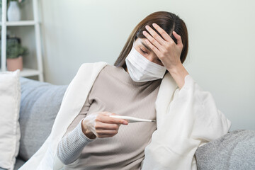 Sick, influenza asian young woman wearing face mask, have fever hand touching forehead, holding...