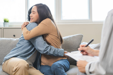 Happy asian young couple love, wife encouraging husband embrace showing hug after consulting problem mental health together with psychologist at clinic. Psychologist with patient sick mental therapy.