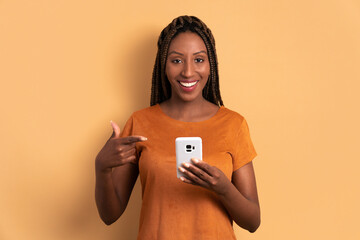 cheerful brazilian woman smiling and holding mobile phone in beige background. app, social media,...