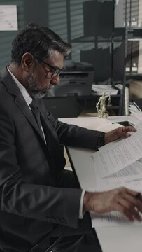 Vertical side footage of male Biracial solicitor in glasses and expensive suit checking and rereading legal contract before cigning it during workday in office