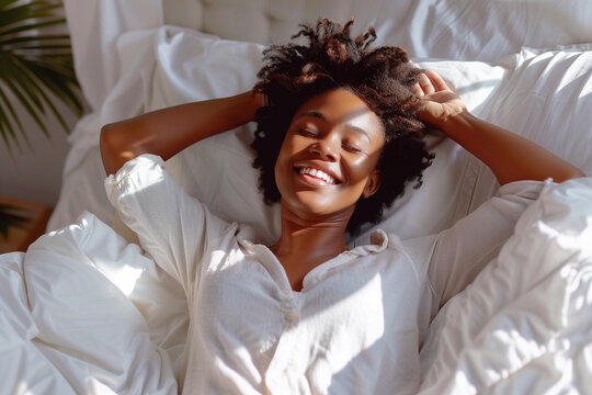 Cheerful African Woman Lying in Bed and Stretching Her Arms – Morning Routine and Wellness Concept. joyful African woman enjoying her morning routine, lying in bed and stretching her arms.