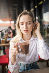 Gen z blonde woman drinks hot chocolate in summer cafe. Tasty beverage and break concept....