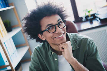 Photo of cool smart employee wear khaki shirt eyeglasses arm hand chin smiling indoors workstation...