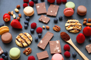 Macarons, chocolate, cookies, berries and various nuts on dark blue background. Selective focus.