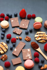 Macarons, chocolate, cookies, berries and various nuts on dark blue background. Selective focus.