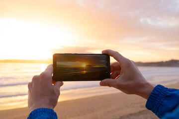 Hands taking photos with a phone at sunset. Galicia Spain.