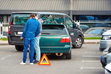 Car accident in parking lot, men set up red warning triangle after collision in parking area....