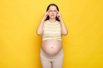 Sick Caucasian pregnant woman with bare belly wearing casual top isolated over yellow background...