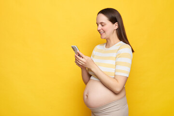 Brown haired smiling Caucasian pregnant woman with bare belly wearing casual top isolated over...