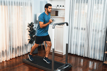 Athletic and sporty man running on running machine during home body workout exercise session for...