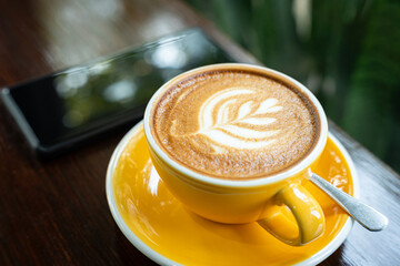 Hot coffee latte with latte art milk foam in cup mug,smartphone on wood desk on top view. As...
