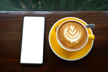 Hot coffee latte with latte art milk foam in cup mug,smartphone with empty screen on wood desk on top view. As breakfast In a coffee shop at the cafe,during business work concept,vintage style