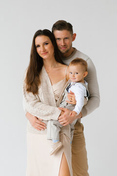 Happy family of three, a man, a woman and a baby, are passing for a picture in the studio on a white background