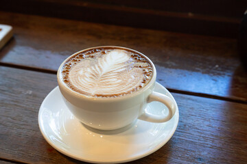 Hot coffee latte with latte art milk foam in cup mug on wood desk on top view. As breakfast In a coffee shop at the cafe,during business work concept,vintage style