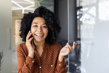 A cheerful young businesswoman engaging in a pleasant conversation on her mobile phone, standing...