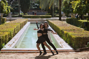 Couple of Latin women, young, dancing bachata with a beautiful fountain in the background in an outdoor park, performing different dance figures. Concept dances, urban, latin.