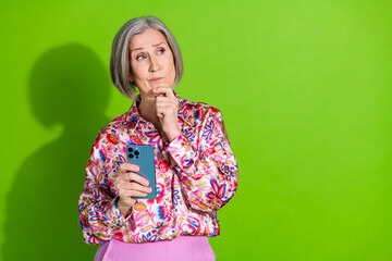 Photo of doubtful unsure lady pink shirt chatting modern device looking empty space isolated green color background