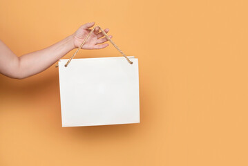 A girl's hand holds a beige paper bag on gold laces on yellow background, the girl has been using paper eco-friendly bags for a long time, the concept of shopping