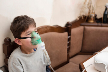 A young boy, 9 years old, inhales medicine through an inhaler, a nebulizer and is happy that he will soon be healthy and will be able to walk with friends on the street, the concept of health