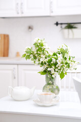 Spring morning in light kitchen: bouquet of white flowers, white teapot and glass of green tea.