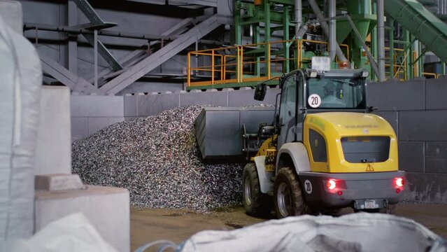 A loader or a Backhoe moves a pile of waste to a garbage factory. A special machine or bulldozer loads garbage at a waste recycling plant. A large pile of plastic and metal, sorting.