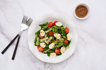 Fresh healthy vegetable salat: cucumber, tomatoes, spinach, couscous, quail eggs, flax seeds on marble background. Top view.