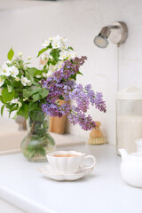 Spring morning in light kitchen: bouquet of white flowers, white teapot and glass of green tea.