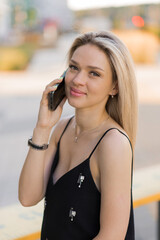 Fototapeta premium Young caucasian woman walking down street with phone, talking with someone, makes a call, has telephone conversation