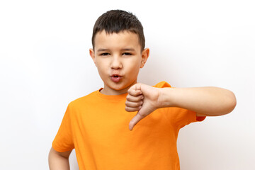 A boy in an orange T-shirt on a white background shows a thumbs down gesture. Sincere children's...