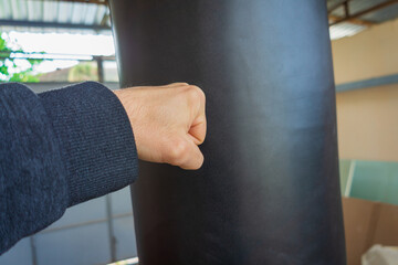 A man's left hand hits a black punching bag. Lifestyle associated with active movement, sports,...