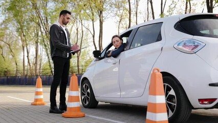 Arabic man driving instructor taking some notes about the passing of the driving test or the exam. Woman improves parking skills during practical courses at driving school