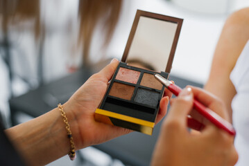 Woman applies makeup with a red brush. She has a small makeup palette in her hands