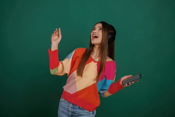 Feel the rhythm, listening to the music. Young woman is standing against green background in the studio
