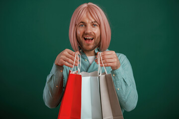 Holding shopping bags. Gay man with pink hair is standing against green background