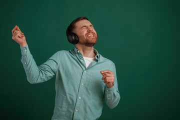 Smiling, enjoying music. Man is standing against background in the studio