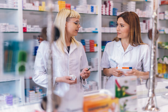 Two young pharmacists at the cash desk of pharmacy store. Talking about medicine.