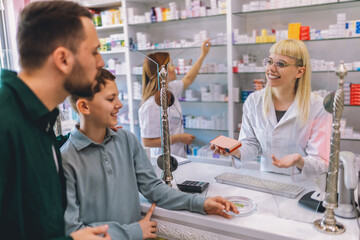 Woman, pharmacist consulting father and son at counter for prescription drugs or medicine at the...