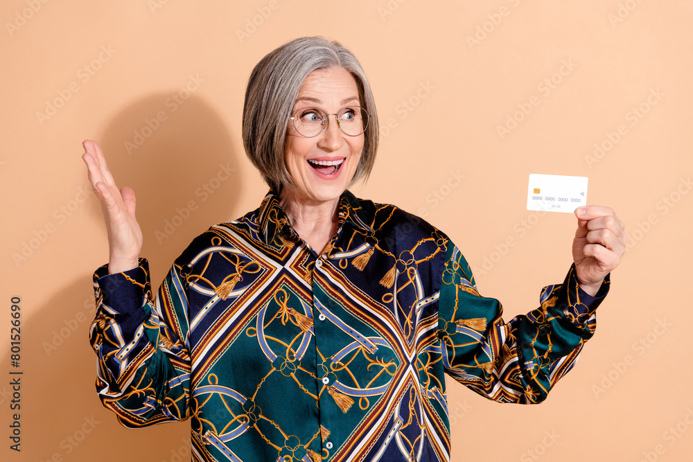 Sticker Photo of overjoyed person wear print blouse in glasses astonished staring at debit card in hand isolated on beige color background