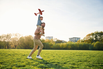 Orange colored toy plane, playing. Happy father with son are having fun on the field at summertime