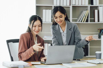 Two young Asian business woman talk, consult, discuss working with new startup project idea presentation analyze plan marketing and investment in the office.