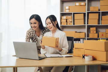Asian businesswoman using laptop computer checking customer's shipping box online at home. SME startup. Small business entrepreneur, freelancer. Online business, SME work